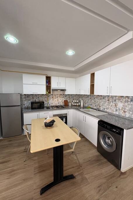 Cuisine en L, façades blanches, lave-linge intégré et réfrigérateur