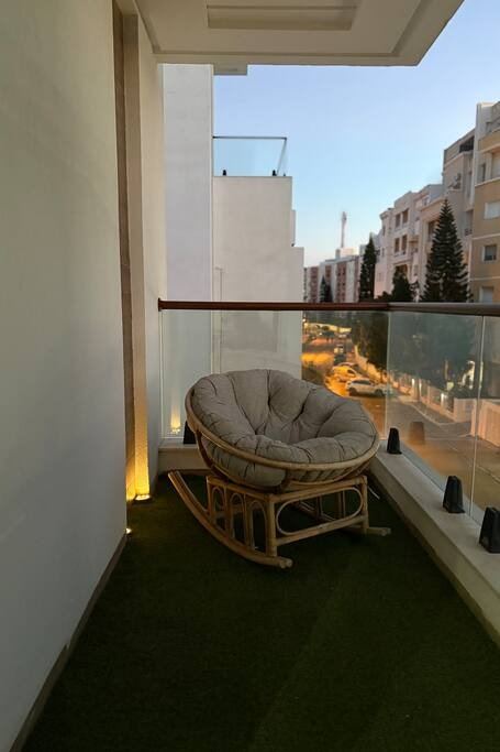 Le balcon en plein jour, fauteuil rond en rotin et vue dégagée sur le quartier